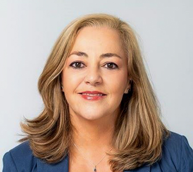 Persona con el cabello a la altura de los hombros que viste un saco y una blusa clara, fotografiada en un espacio interior frente a un fondo liso de color claro, en una imagen de retrato en primer plano.