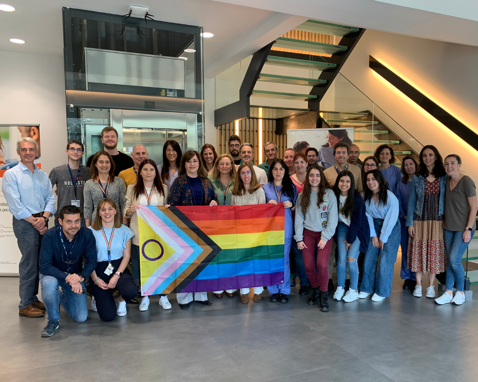 Grupo de asociados de BD de pie juntos en interior sosteniendo una bandera del Orgullo.