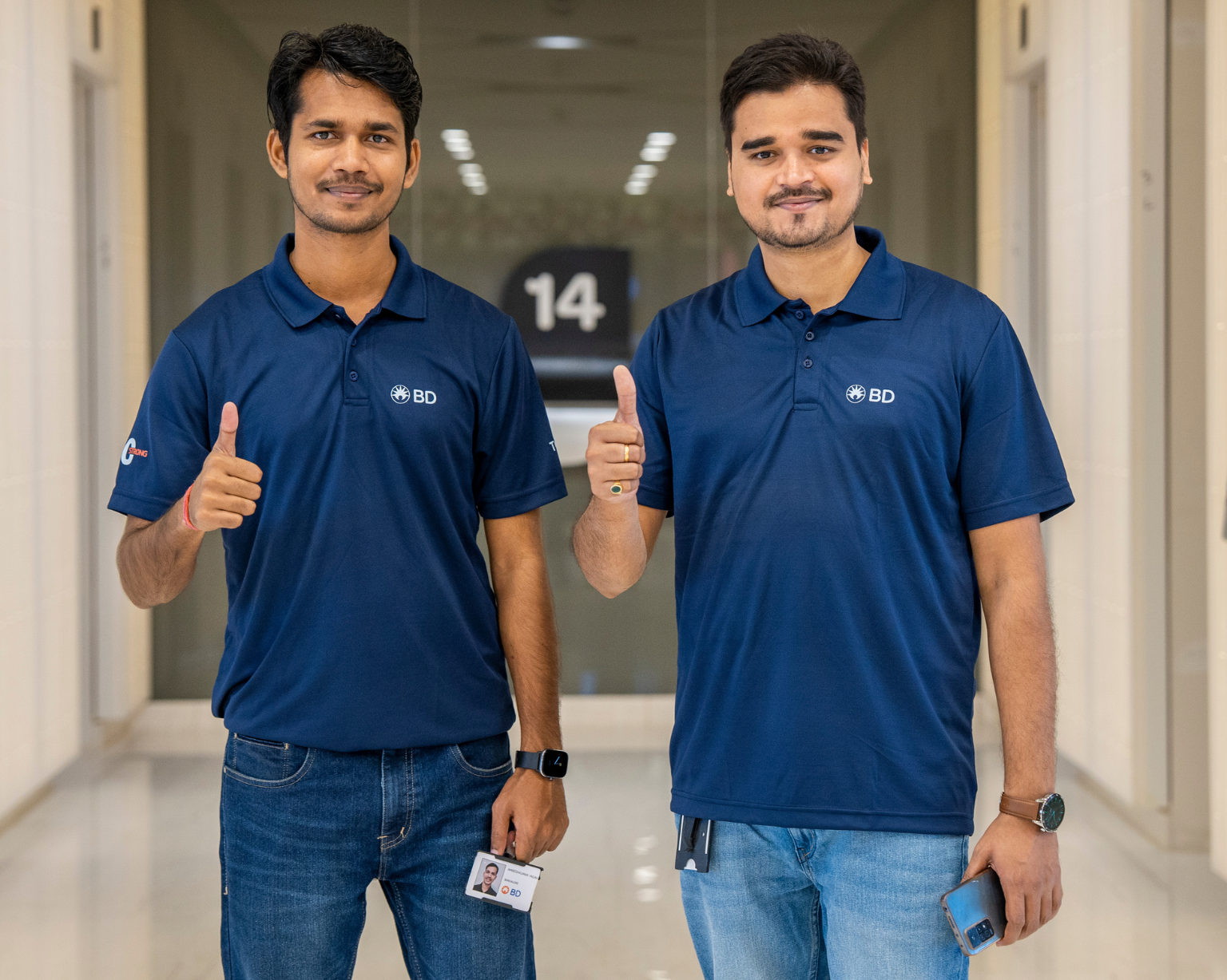 Two BD associates standing in a hallway giving a thumbs‑up.