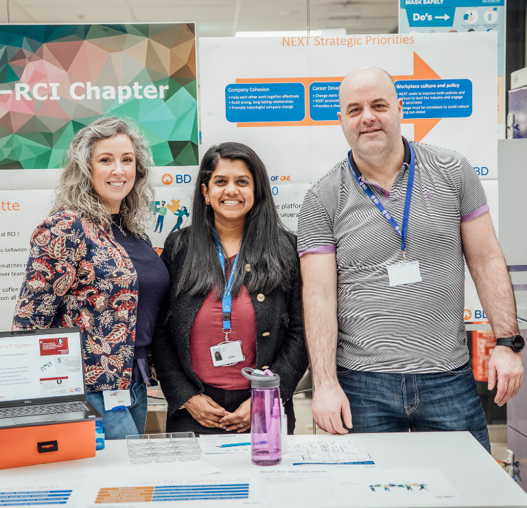 Three BD associates standing behind an inclusion-focused information booth at a workplace event.