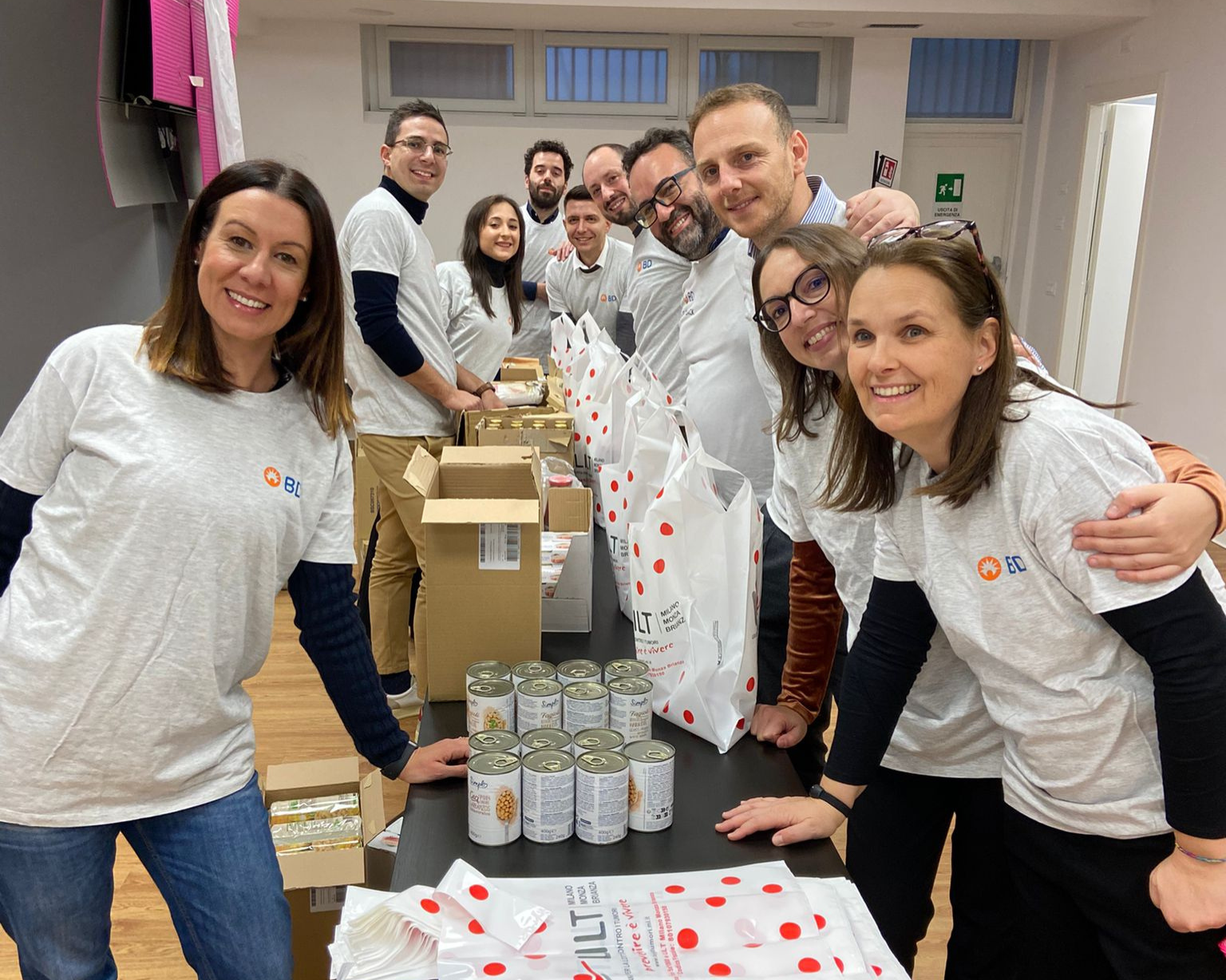 Group of BD associates standing together indoors packaging food donations at a team volunteer event.