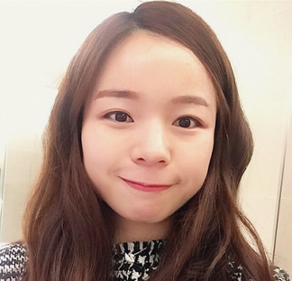 어깨까지 내려오는 짙은 머리를 가진 개인이 카메라를 향해 미소 짓고 있는 인물 사진.