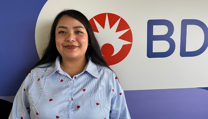 Asociado de BD de pie frente a una pared con la marca BD.