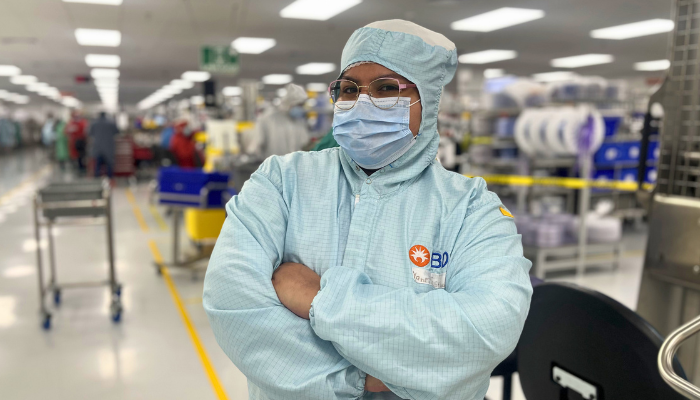 Asociado de BD con vestimenta de sala limpia dentro de una planta de manufactura.