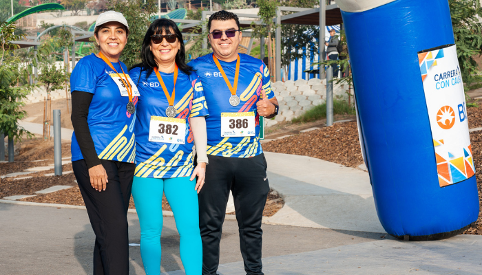 Tres asociados de BD usando medallas en un evento comunitario de carrera.
