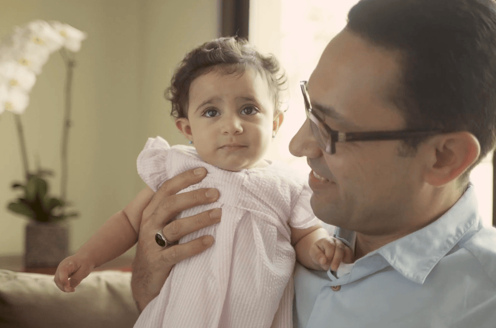 Father holding his baby daughter indoors while smiling in her direction.