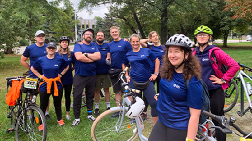 Group of ten people wearing navy shirts and posing outside around a few bikes. Some people are wearing helmets.