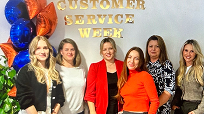 A group of six people wearing business attire, smiling at the camera, standing a BD office.