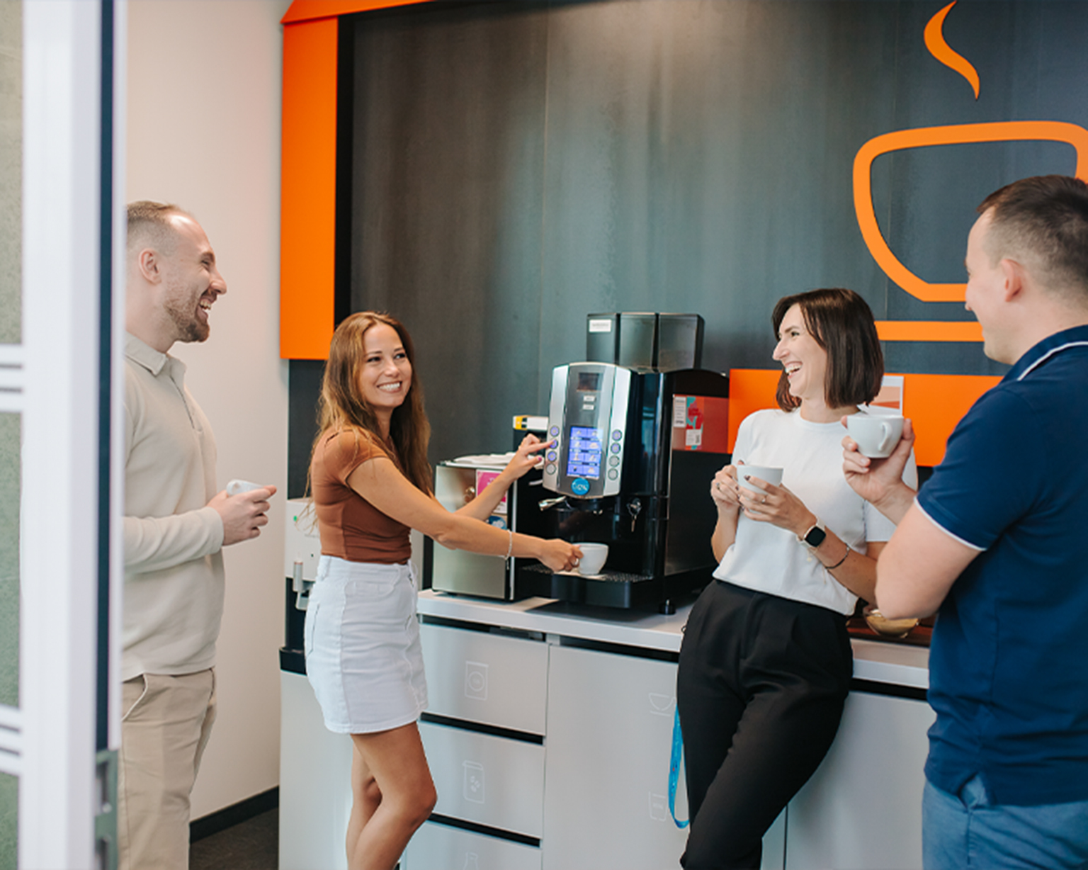 Group of BD associates chatting and having coffee in a modern office break area.