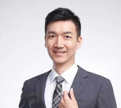 Portrait-style photo of a subject wearing a grey suit jacket, tie and white collared shirt, smiling at the camera.
