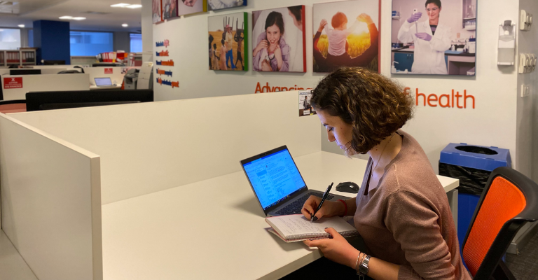 BD associate working at a desk with a laptop and notebook in a BD office workspace.