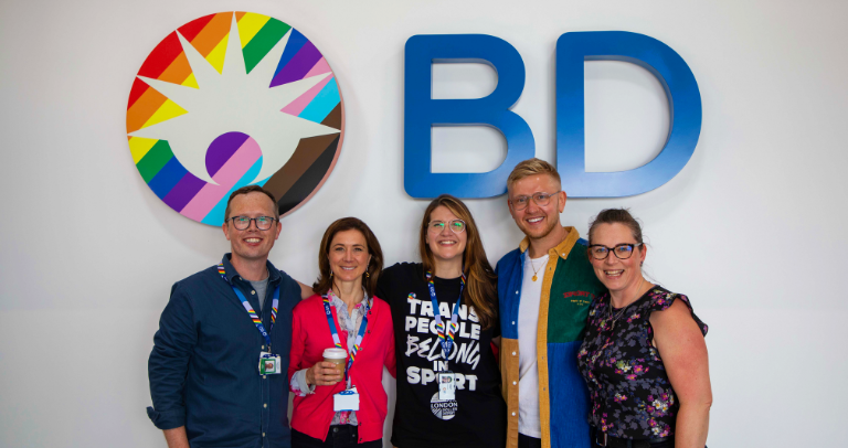 Group of BD associates standing together in front of a BD logo during Pride Month.