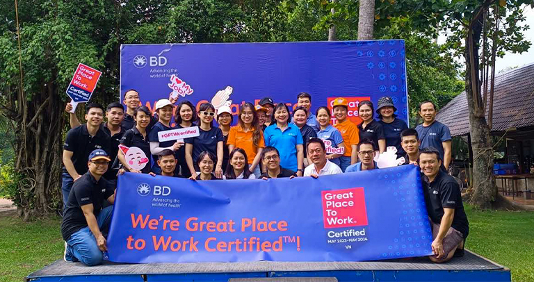 Large group of BD employees posing with Great Place to Work Certified signage at an outdoor event