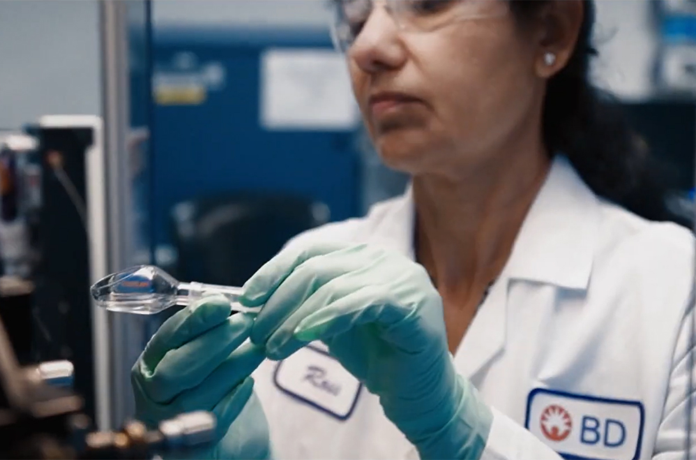 Cientista usando luvas e óculos de segurança, segurando um dispositivo médico.