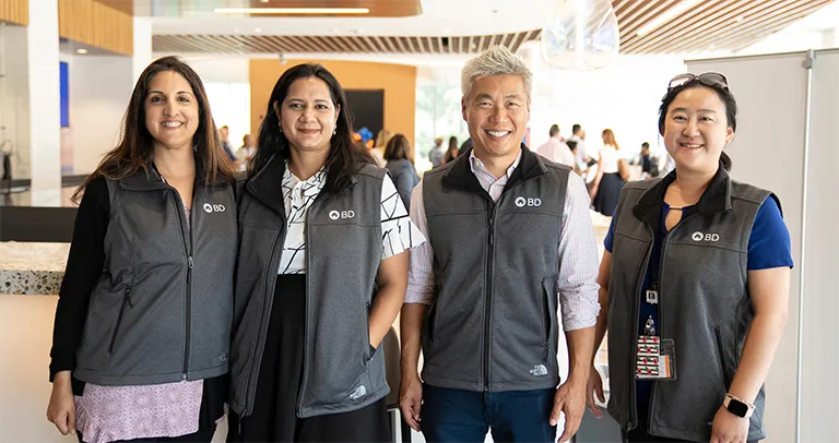 Cuatro asociados sonriendo, vistiendo chalecos a juego con el logotipo de BD.