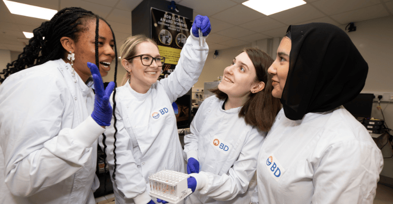 Quatro engenheiros sorrindo, com um deles segurando um tubo de ensaio