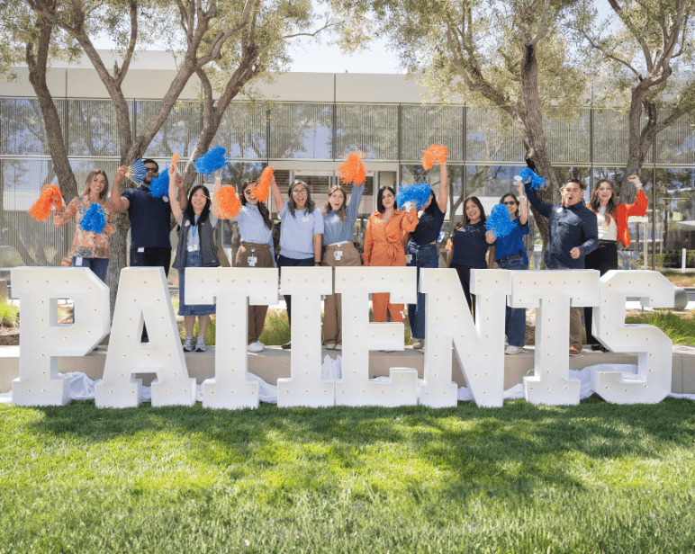 Outdoor photo of lots of BD associates all cheering together in front of a sign which reads 'Patients'.