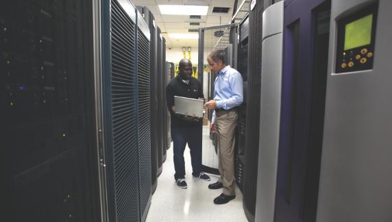 Dos asociados de pie juntos, junto a grandes servidores inform&aacute;ticos.