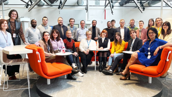 Un grupo numeroso de asociados sonriendo a la c&aacute;mara en un espacio de oficina.