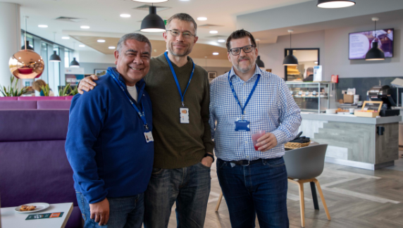 Tres personas sonriendo juntas a la c&aacute;mara en una cafeter&iacute;a.