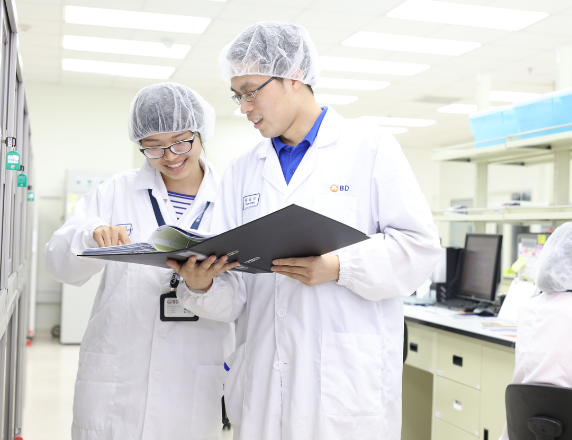  白衣を着た2人の科学者が、一緒にノートを読んでいる。