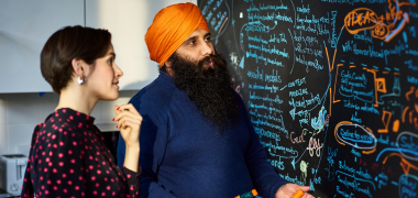A man and woman looking at a whiteboard full of text and diagrams