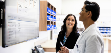 A woman smiling at a pharmacist who is looking at a screen
