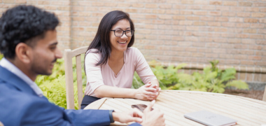 A smiling man and woman sat outside at a table