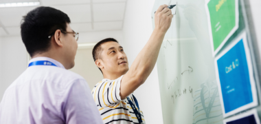 A man watching another man write on a whiteboard