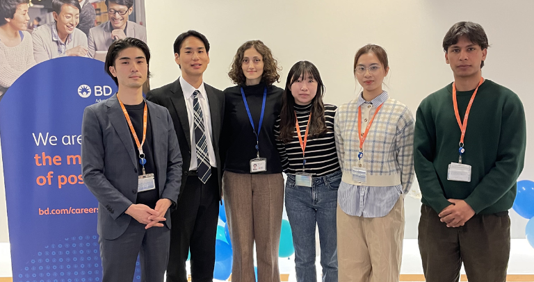 BDのバナーの前で並んで立つ、名札を着用したアソシエイトたち。