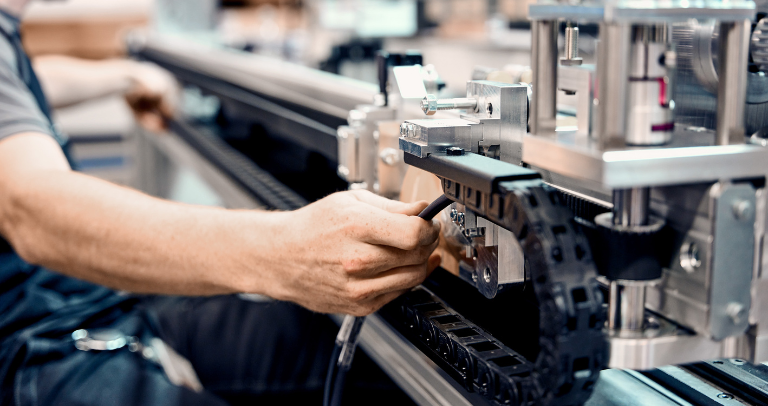 狭い作業スペースのある工業用の作業環境で、大型の自動化装置の内部部品を一緒に作業する2人。