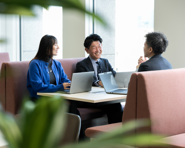 Individual wearing a high‑visibility orange safety vest and cap standing inside a warehouse with shelving and charts in the background.