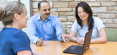 Three people sitting around laptop on table