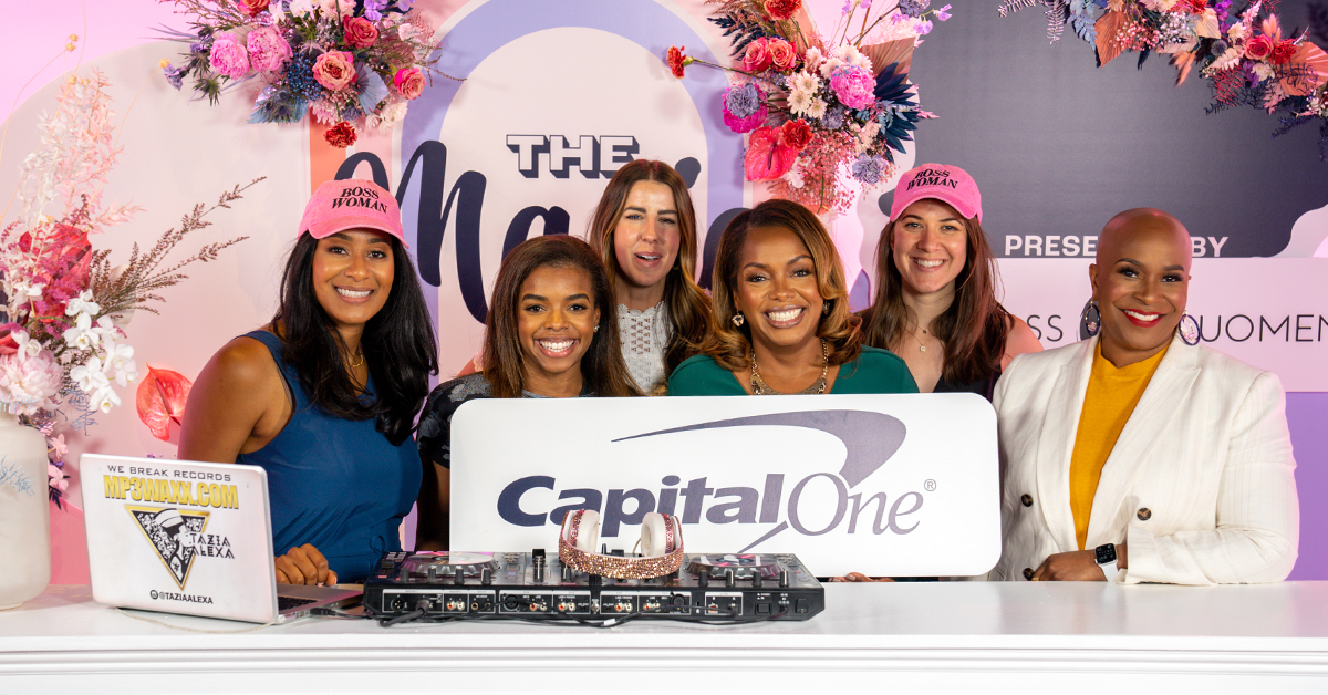A group of Capital One associates stand in front of a blue and pink backdrop at the Black Girl Magic Digital Summit, holding a Capital One sign