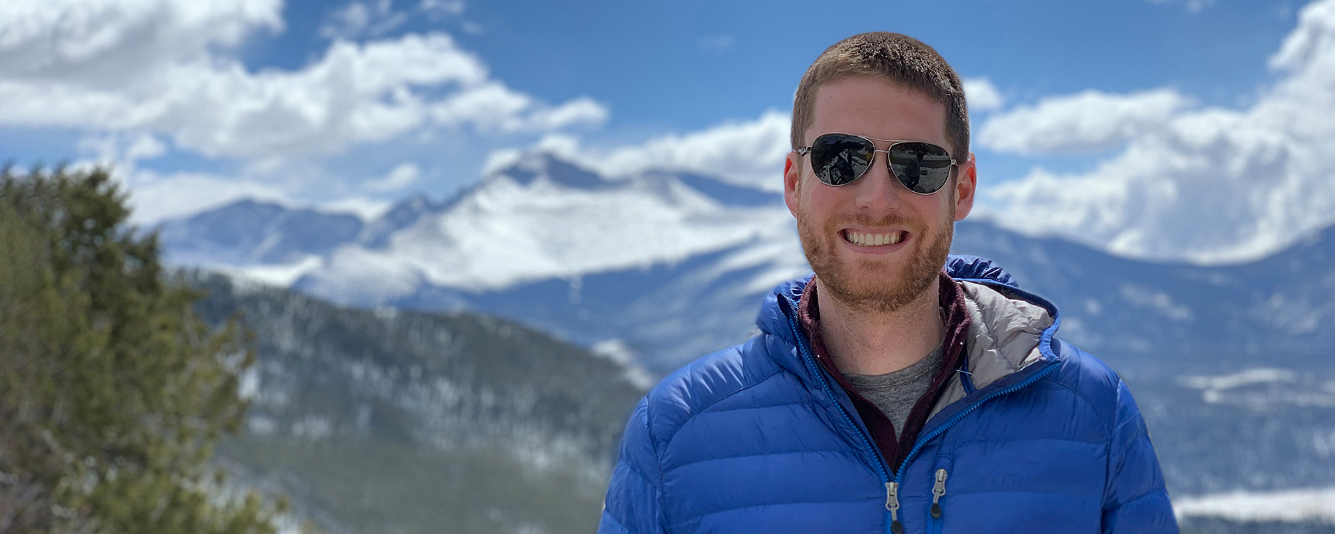 Jared, a Capital One tech associate, stands in front of snowy mountaintops