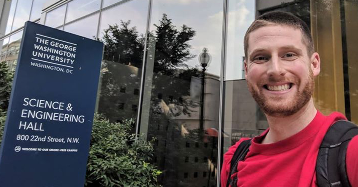 Jared, Capital One tech associate, stands in front of the Science & Engineering Hall sign at at George Washington University (GW) where he received his Masters in Computer Science