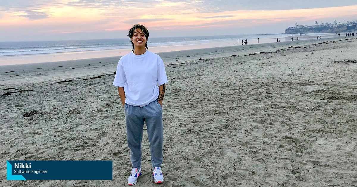 Nikki, Capital One Software Engineer, stands on a beach and smiles