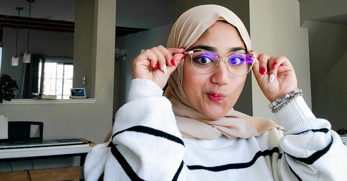 Khadija sits at her home office and makes a silly face holding her glasses