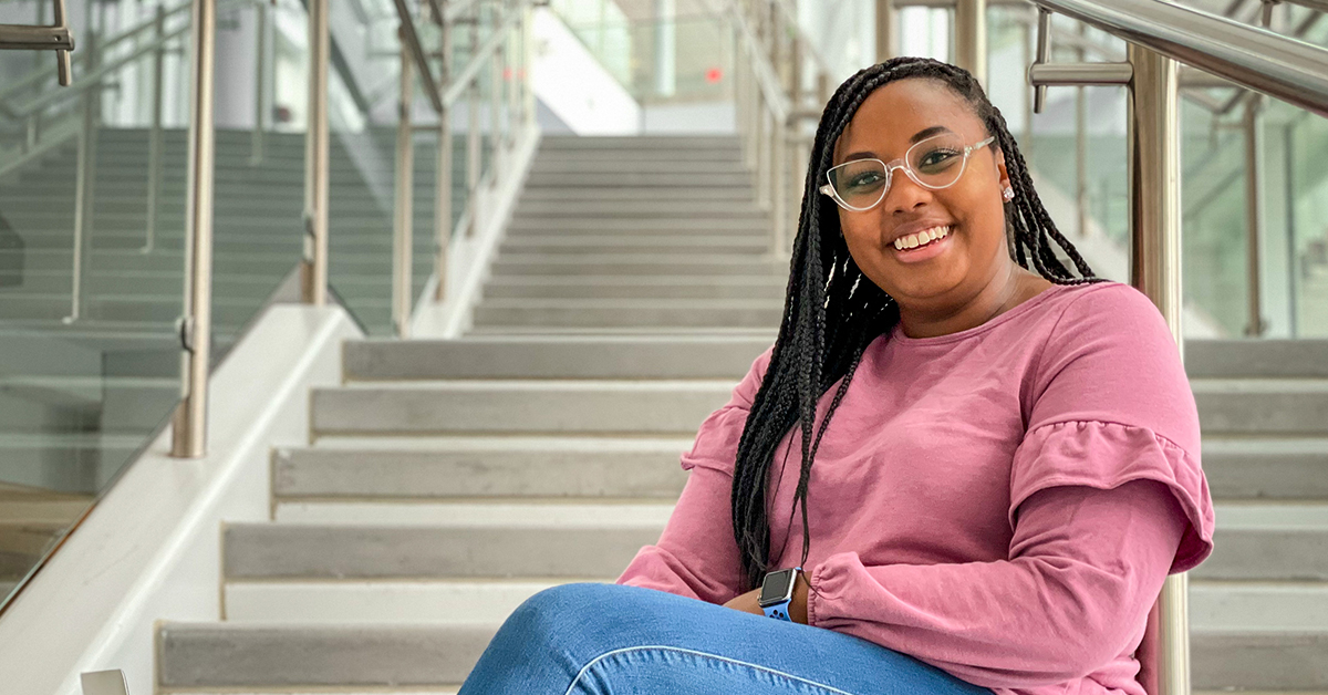 Capital One associate Nyla sits on the stairs and smiles in a Capital One building 