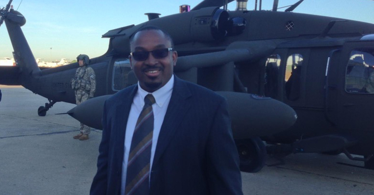 Capital One associate and veteran Lenton stands in front of a military helicopter