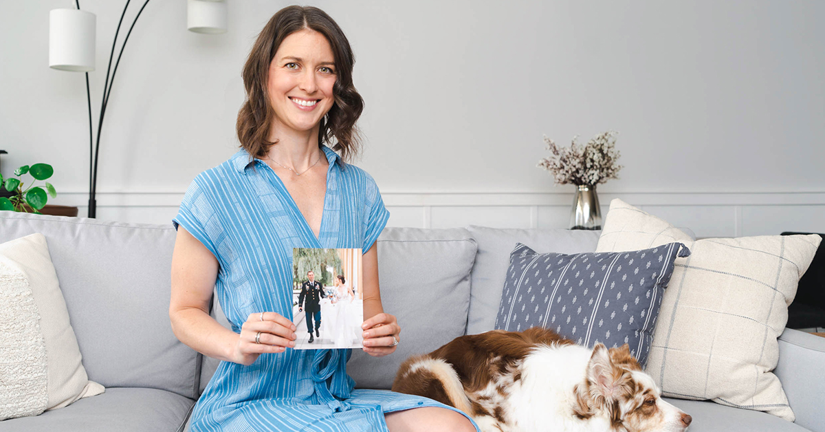 Capital One associate and military spouse sits on her couch with her dog holding a picture of her wedding day with her husband in military uniform
