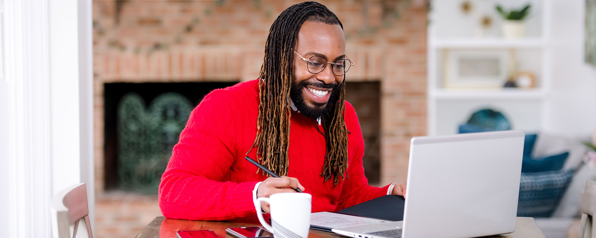 Capital One associate sits in his house in a red sweater on his laptop while working from home