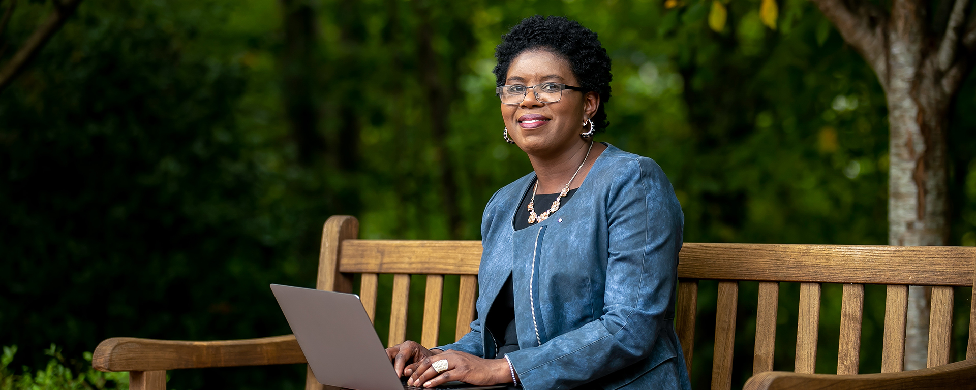 Capital One leader Maureen sits on a bench and smiles with her laptop