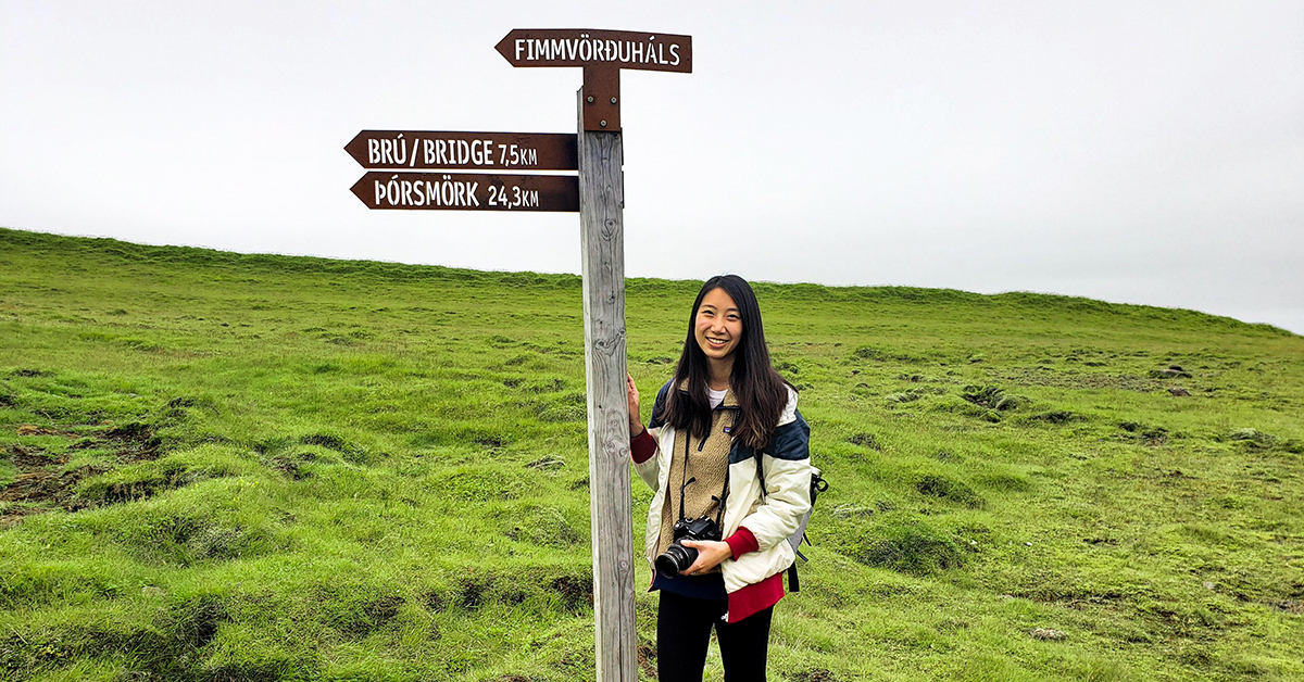 Capital One Green Team Member Allison standing under a sign with foreign street names in a green hilly field