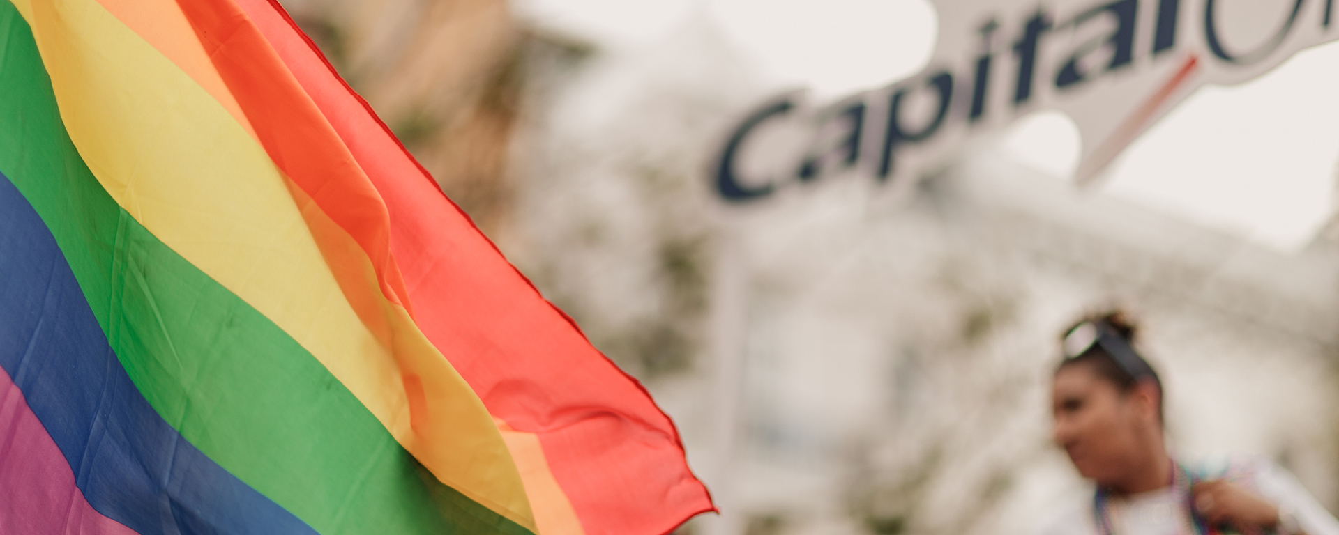 The Pride flag blowing in the wind, with Capital One's logo blurred in the background