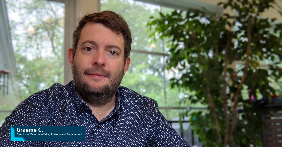 Capital One associate Graeme C., Director of External Affairs, Strategy and Engagement, sitting in front of a window and a tree