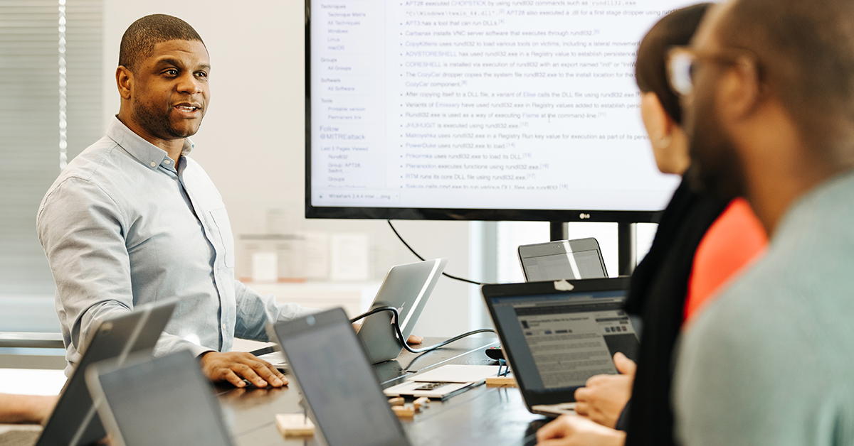 Man stands at laptop and works with his team of Software Engineers at Capital One