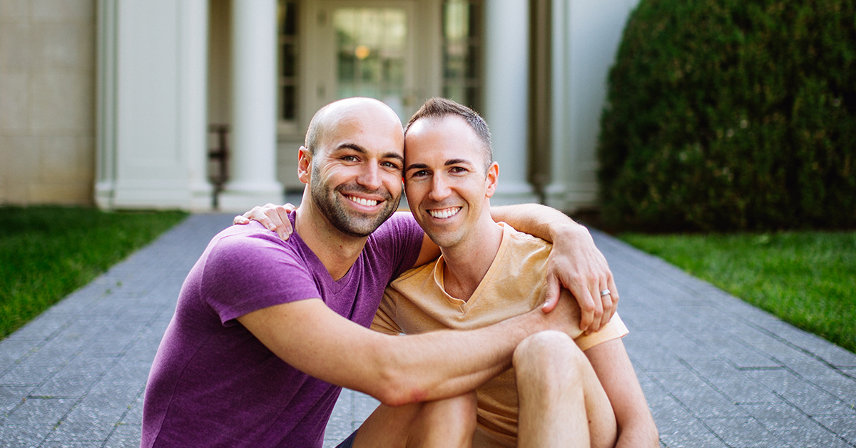 MC, Capital One Director, and his partner sit on a stone pathway in front of a building as he talks about immigrating to the US before same sex marriage was legal