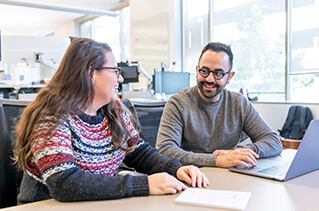 Two employees talking at a table with a laptop computer.