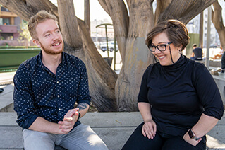 Two employees talking outside at the base of a tree .